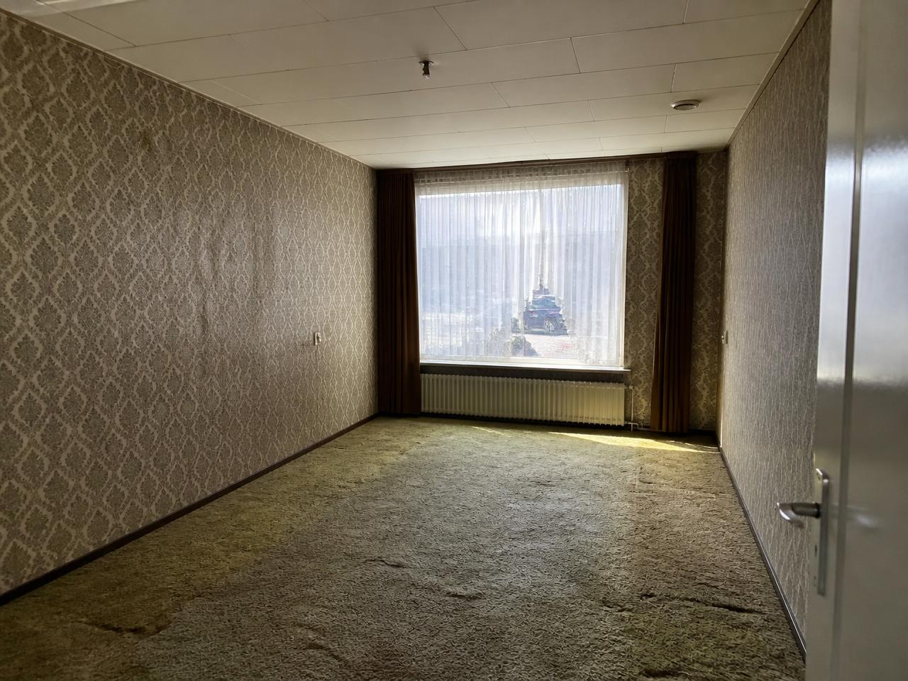 Woonkamer voor de renovatie met oud tapijt en donker behang